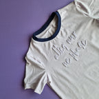 Light lilac t-shirt with blue trim and text on a purple background