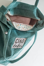 Green corduroy bag with floral interior and 'CIAO' label on a light background