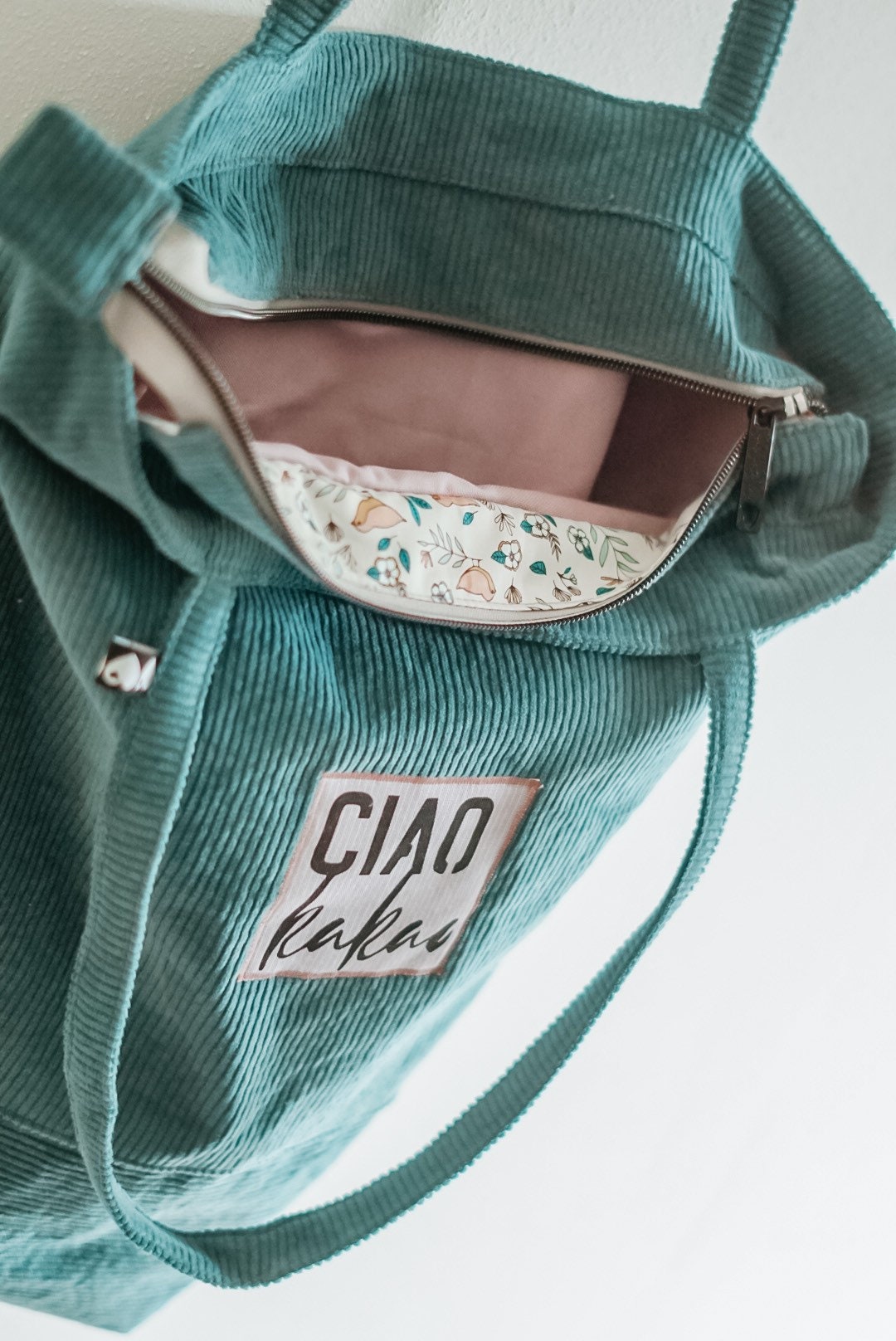 Green corduroy bag with floral interior and 'CIAO' label on a light background