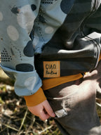Close-up of a child's hand wearing a jacket with a 'Ciao Kakao' label, outdoors.