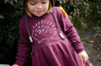 Child wearing a purple dress with a screen printed hedgehog design outdoors